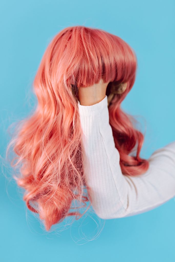 Close-up of a vibrant pink wig held against a blue backdrop, showcasing its wavy texture.