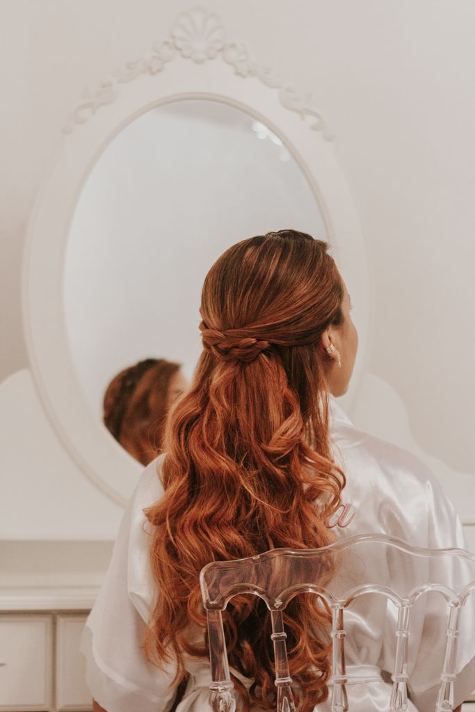 A redhead woman sits in front of a mirror, showcasing her elegant braided hairstyle.