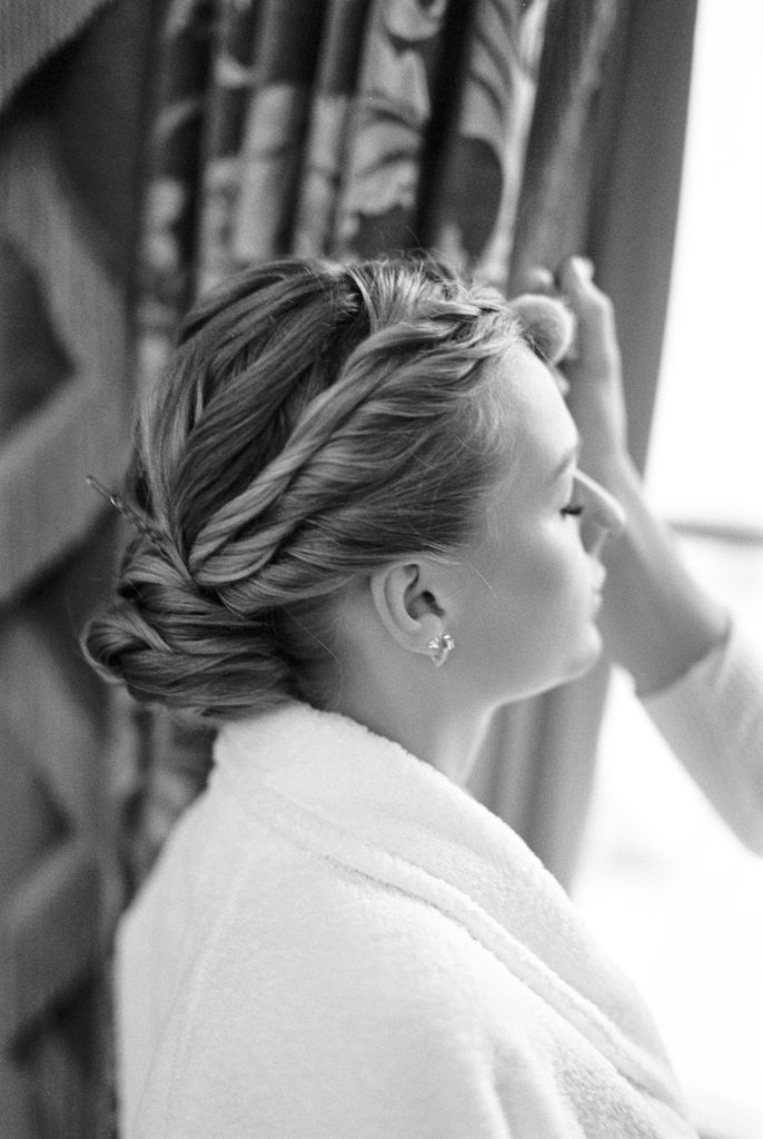 Black and white photo of a bride having her makeup done, emphasizing elegance and poise.